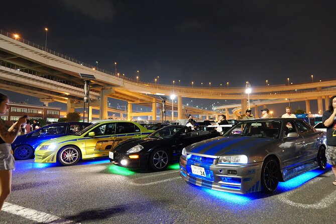 Getunte JDM-Autos mit Neon-Unterbodenbeleuchtung nachts aufgereiht unter dem Autobahnkreuz der Daikoku PA